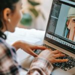 crop ethnic freelancer retouching photo on laptop at home